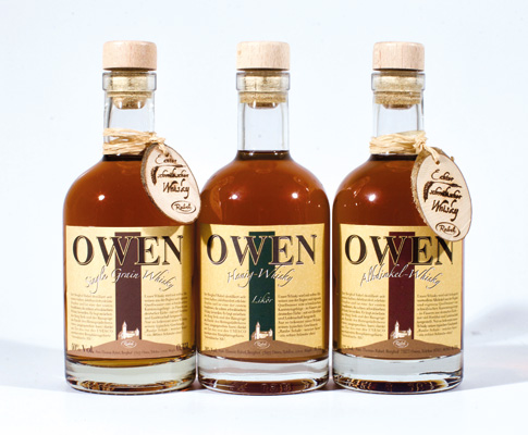 Drei Whisky Flaschen vom Hersteller Owen. Der Hintergrund des Bildes ist weiß. Die Spirituosen haben ein beige Etikett mit großer Aufschrift OWEN.