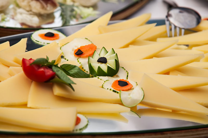 Käsespezialitäten, Käseplatte - Bildinhalt: Silbere Platte belegt mit verschiedenen Käsearten. Als Deko wurden Gurgenblumen mit Karotten und Tomaten sowie Basilikum verwendet.